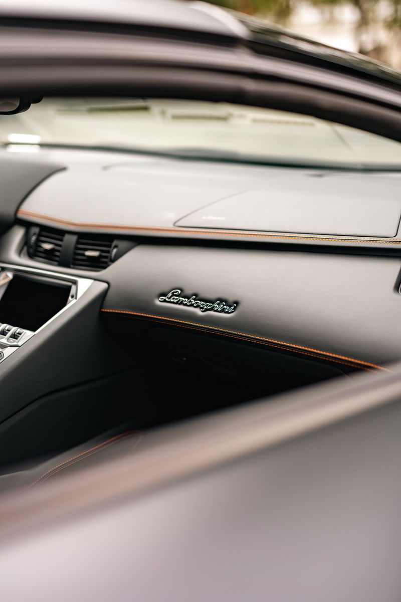 Interior of a black Lamborghini Aventador LP700-4 with orange stitching and embossed logo.