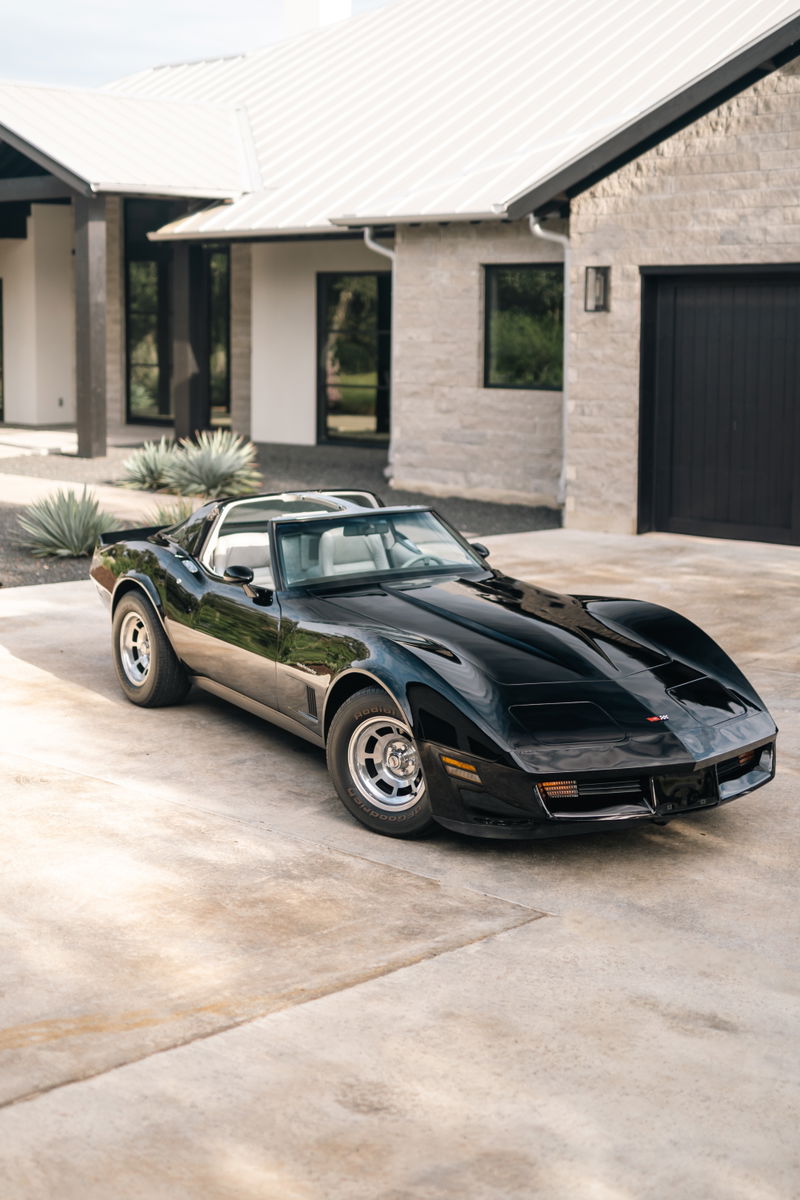 Black 1982 Chevrolet Corvette Stingray T-top with silver rims parked on concrete.