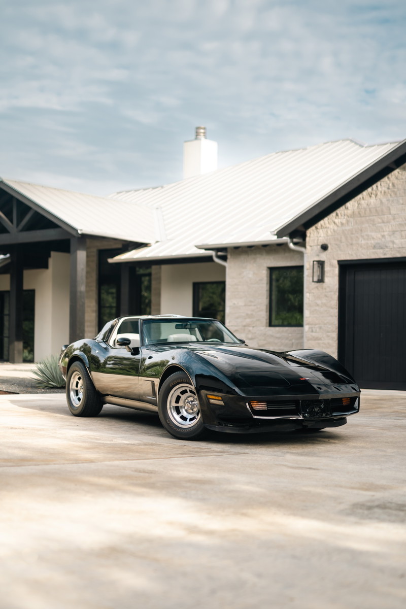 Black 1982 Chevrolet Corvette Stingray with polished aluminum rims parked in front of a modern home.