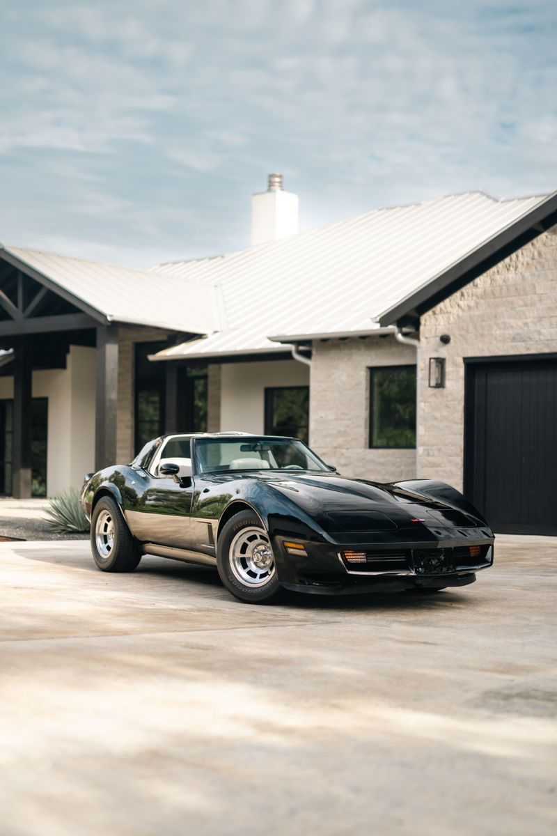 Black 1982 Chevrolet Corvette Stingray with polished aluminum rims parked in front of a modern home.