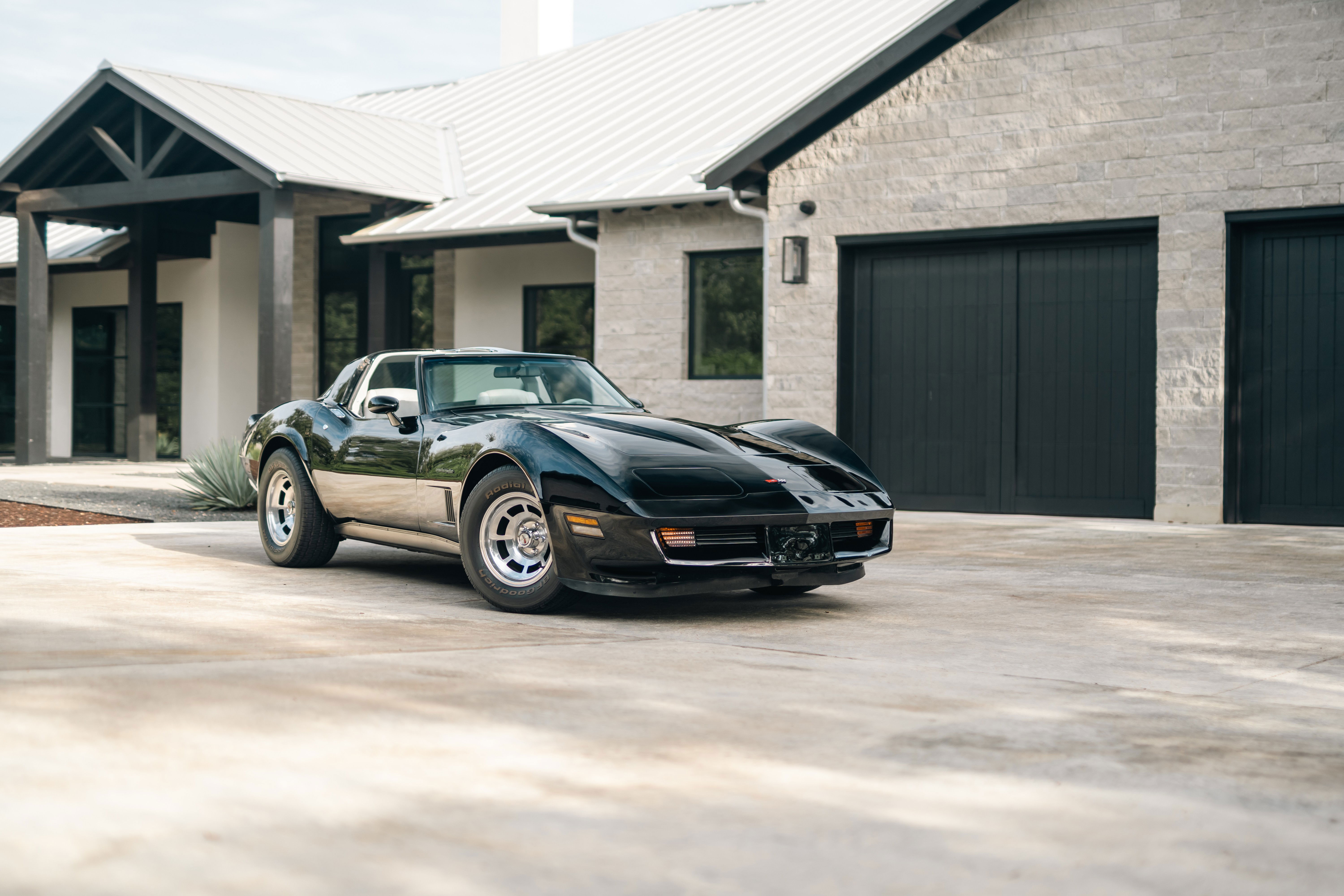 Black 1982 Chevrolet Corvette Stingray with chrome rims parked in front of a modern home.
