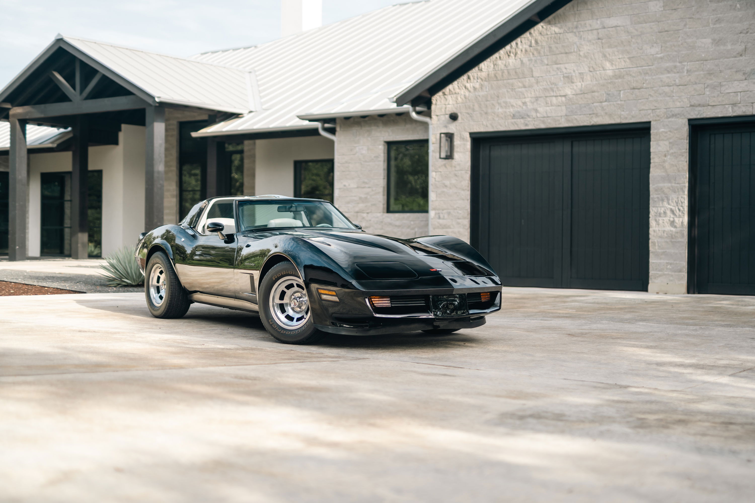 Black 1982 Chevrolet Corvette Stingray with chrome rims parked in front of a modern home.