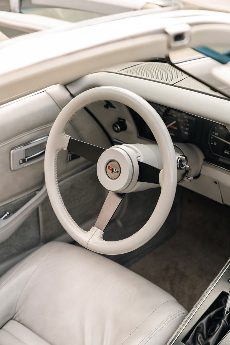 Close-up of a white 1982 Chevrolet Corvette Stingray interior, featuring a white leather steering wheel and seats.