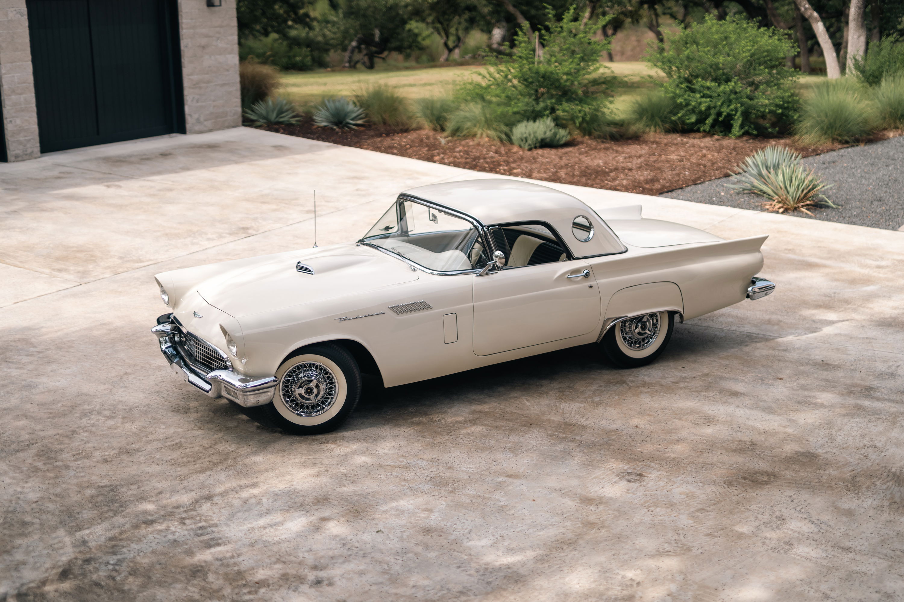 A Colonial White 1957 Ford Thunderbird with wire wheel covers sits in a driveway.