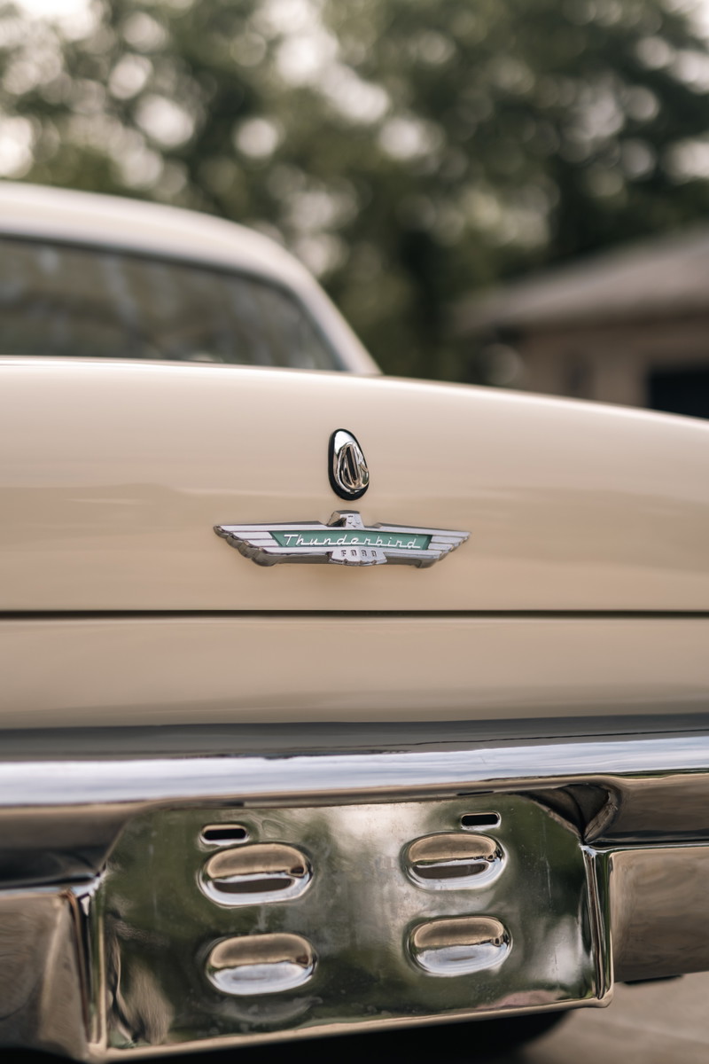 Close up of a colonial white 1957 Ford Thunderbird rear emblem and chrome bumper detail.