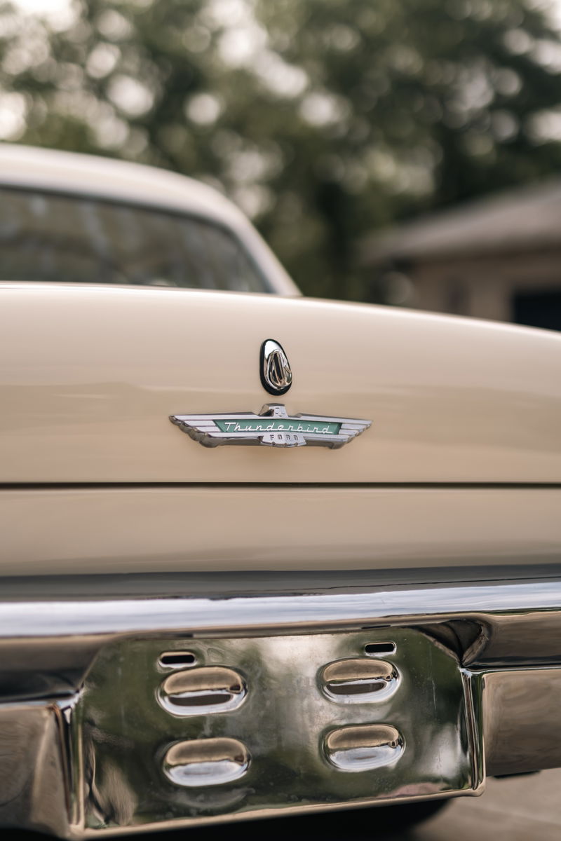 Close up of a colonial white 1957 Ford Thunderbird rear emblem and chrome bumper detail.