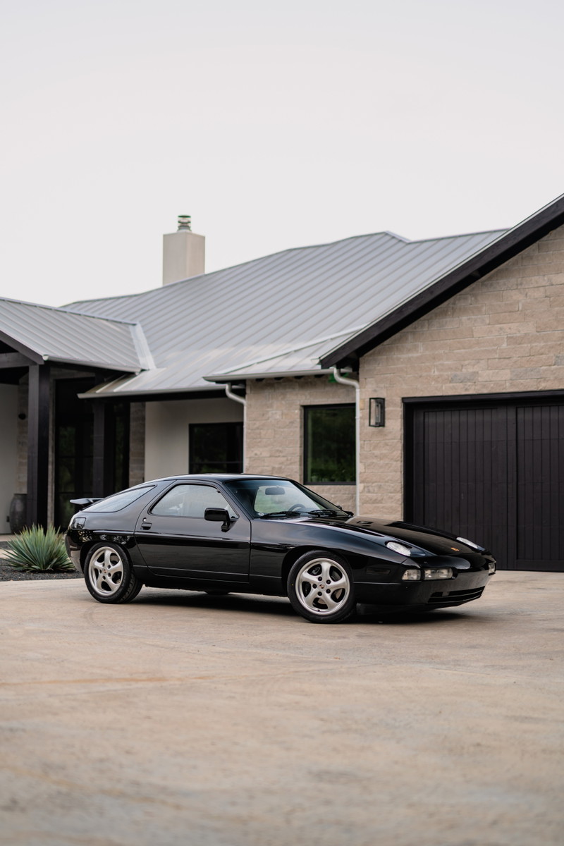 Black 1984 Porsche 928 S4 with silver cup style rims parked in front of a modern home.