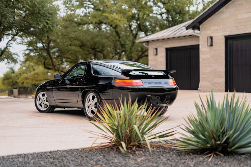 Black 1984 Porsche 928 S4 with silver rims and rear spoiler.