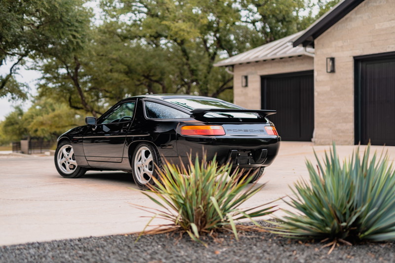 Black 1984 Porsche 928 S4 with silver rims and rear spoiler.