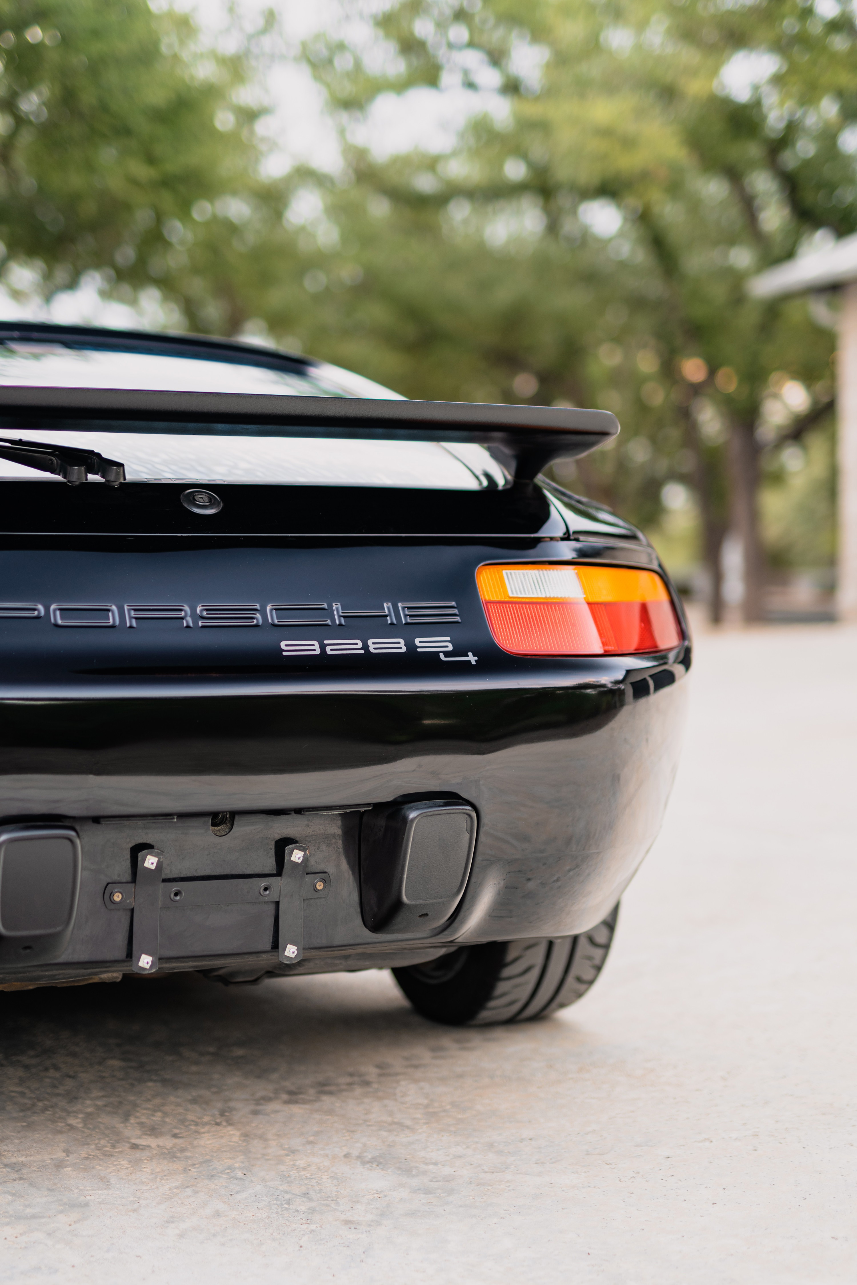 Black 1984 Porsche 928 S4 rear, showing taillight, spoiler, and exhaust.