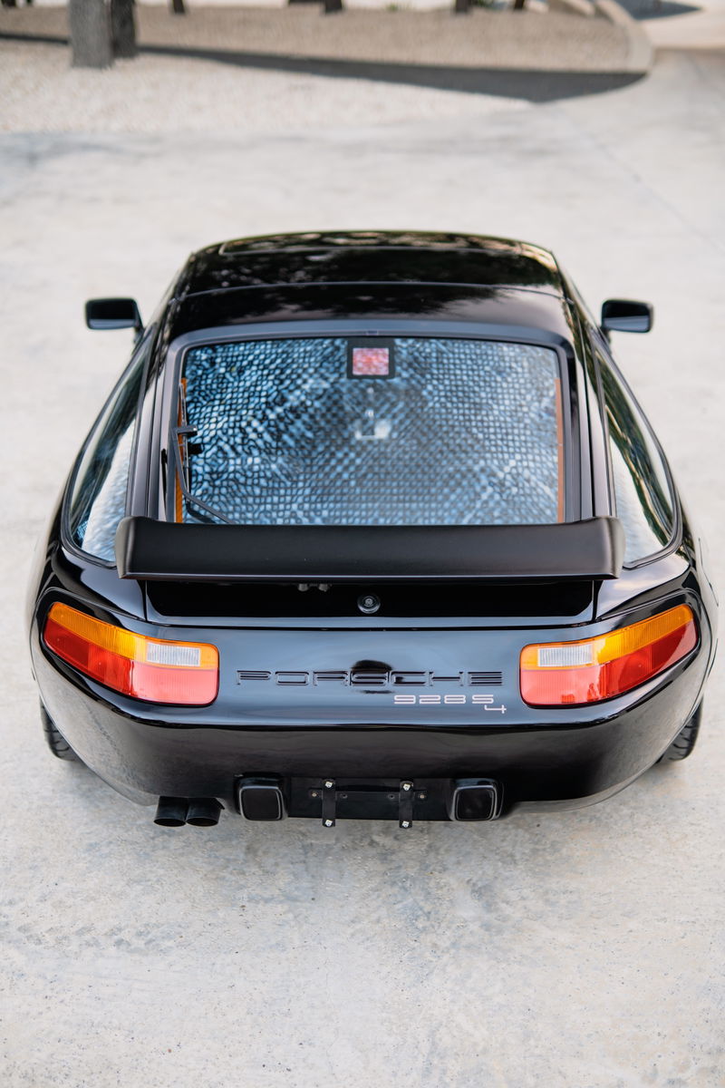 Rear view of a black 1984 Porsche 928 S4 with quad exhaust tips and a rear spoiler.
