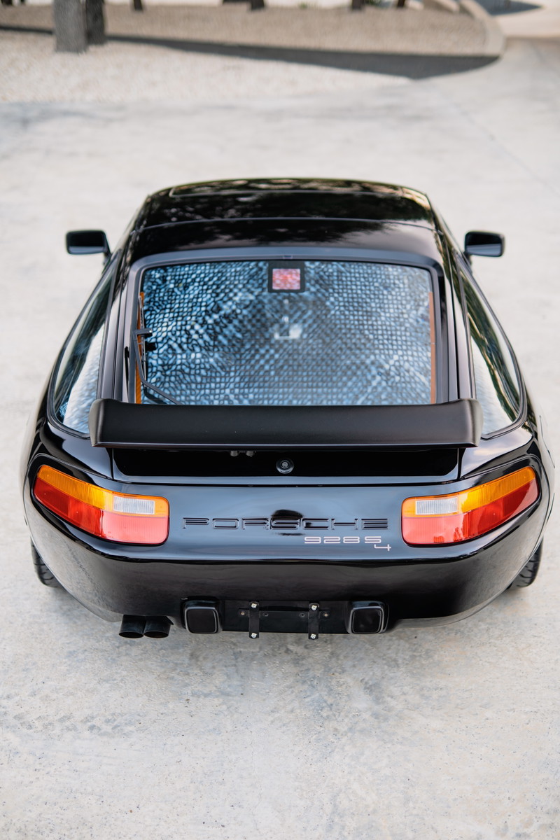 Rear view of a black 1984 Porsche 928 S4 with quad exhaust tips and a rear spoiler.