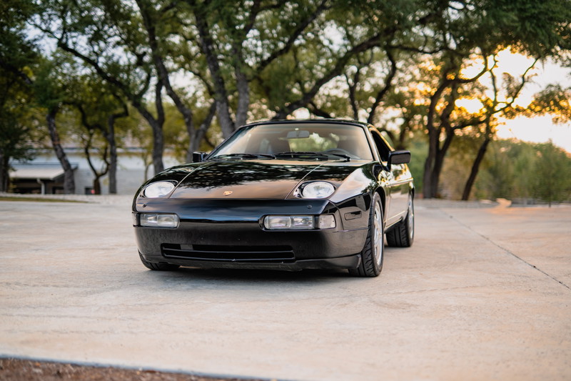 Front view of a black 1984 Porsche 928 S4 with its iconic pop-up headlights and clean trim.