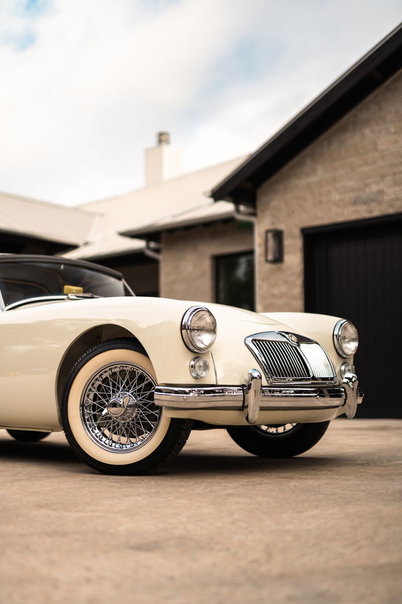 Front view of a cream 1957 MG MGA with chrome wire rims and whitewall tires.