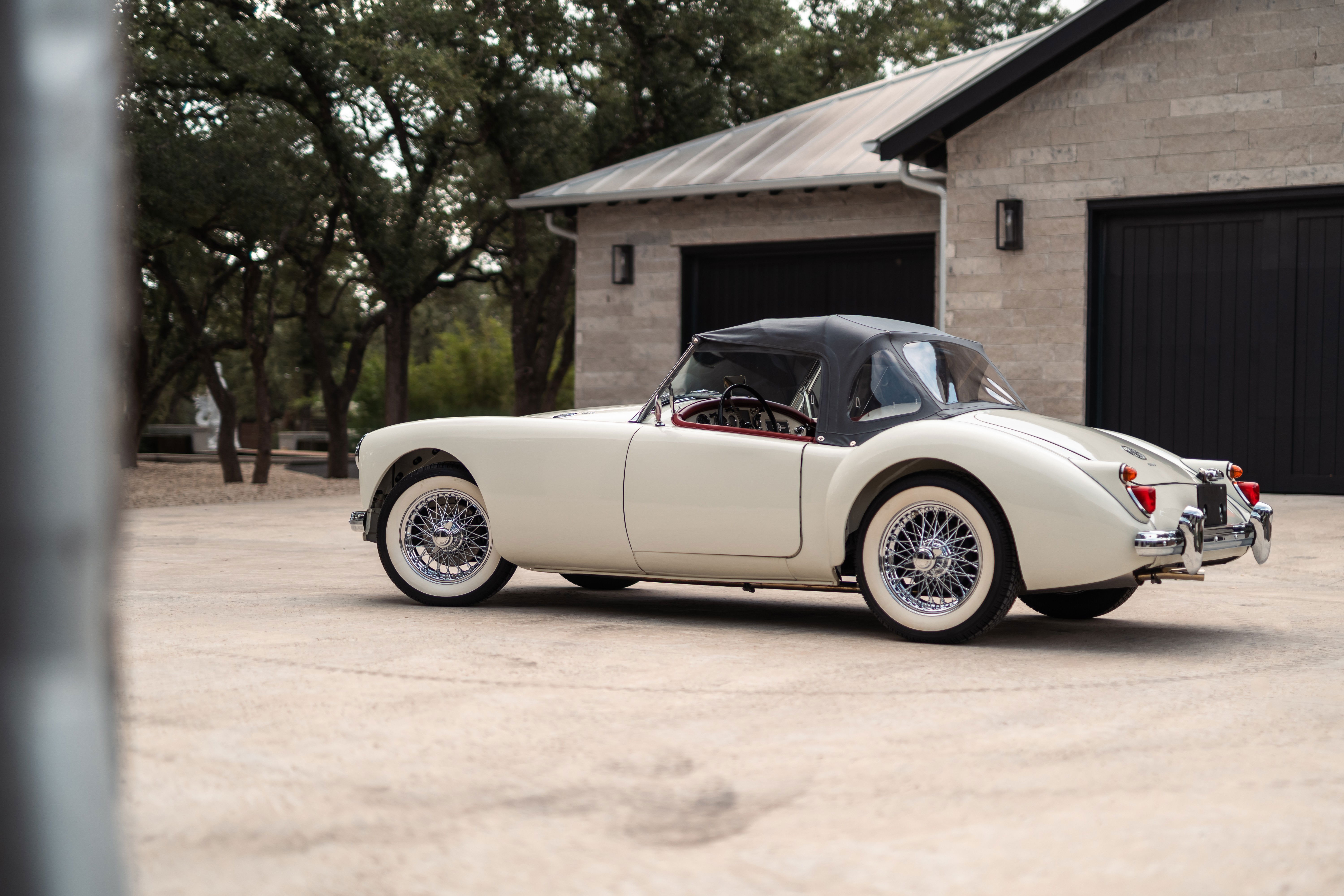1957 MG MGA Roadster in Old English White with wire wheels parked in front of a garage.