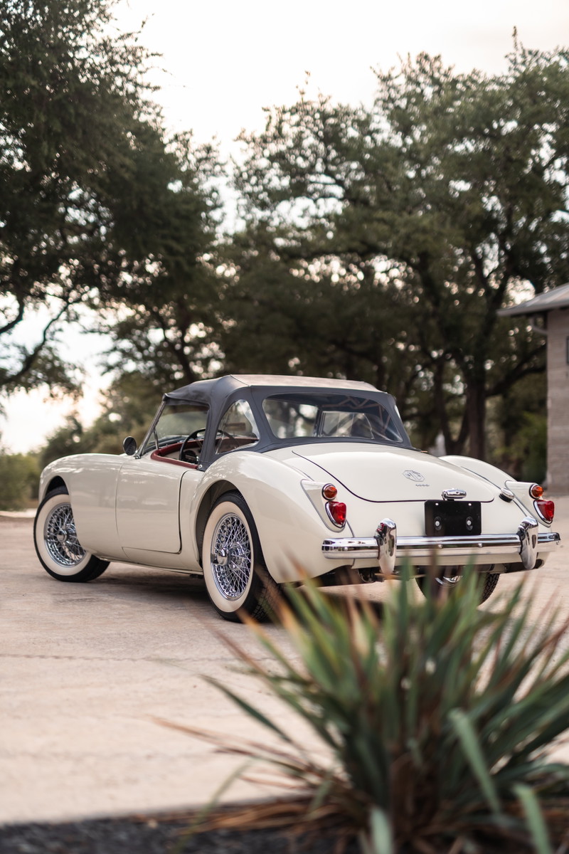 Rear view of a classic Old English White 1957 MG A convertible with wire rims and whitewall tires.