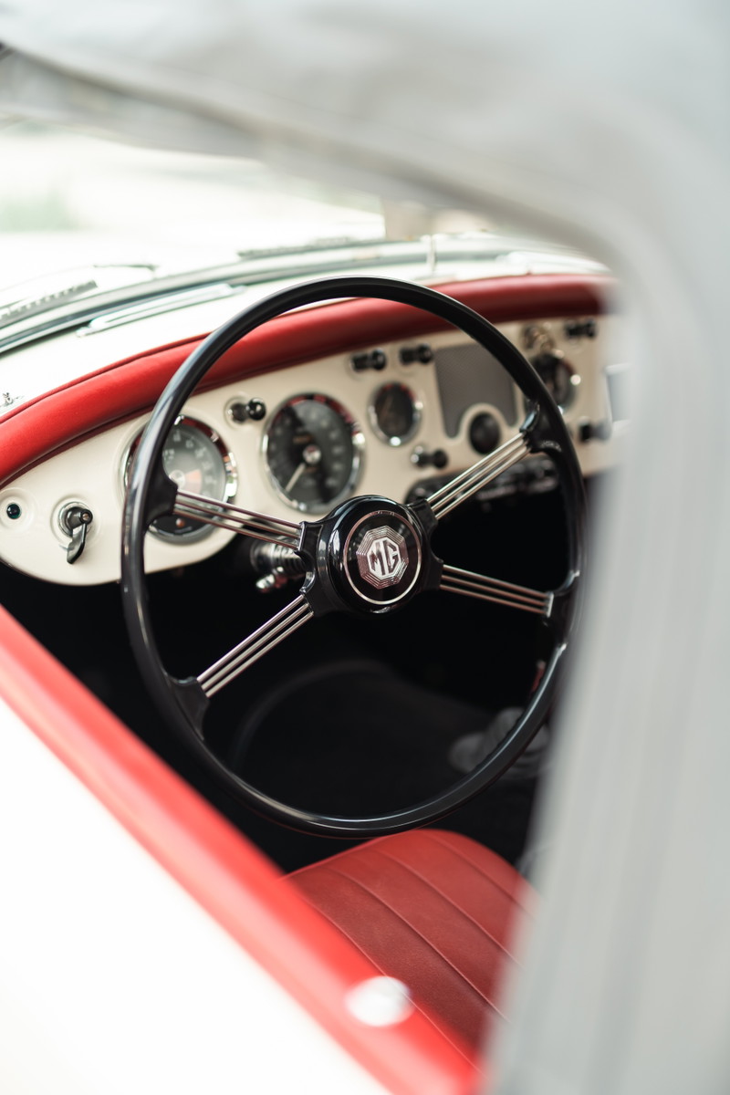 Interior view of a 1957 MG MGA with red leather seats and a black steering wheel with an MG logo.