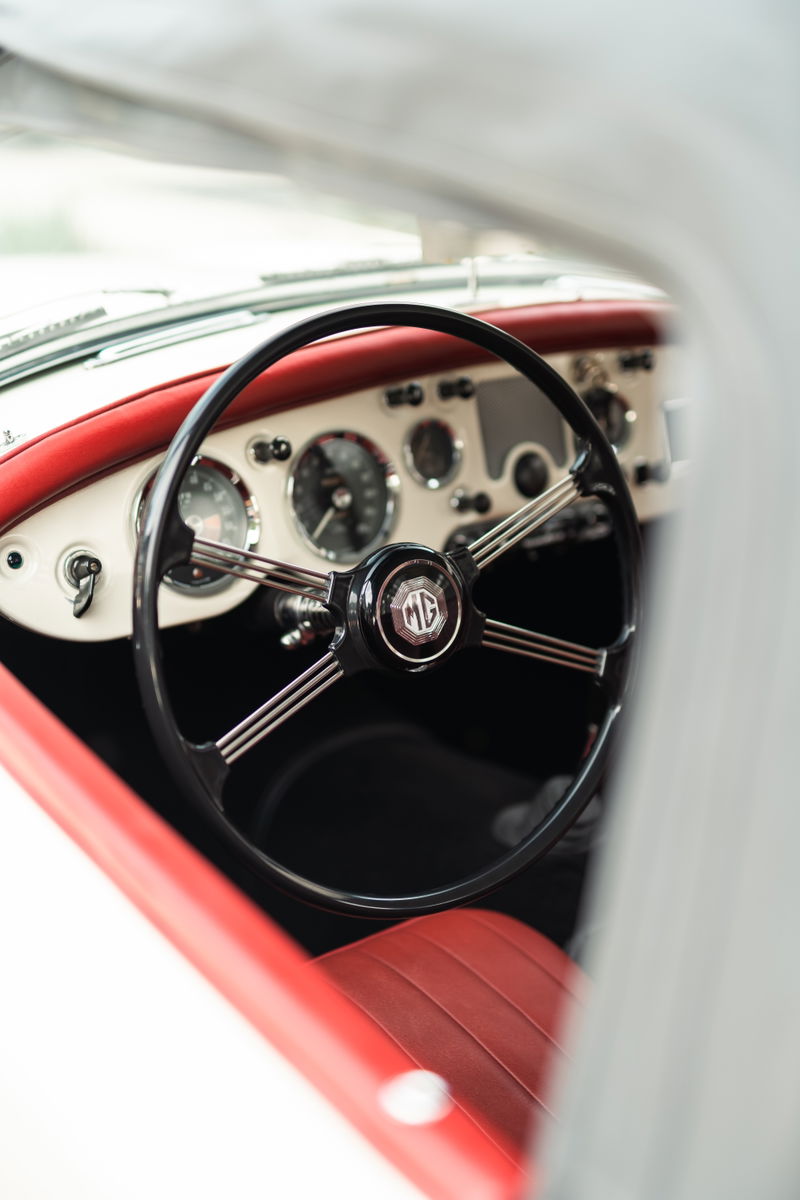 Interior view of a 1957 MG MGA with red leather seats and a black steering wheel with an MG logo.