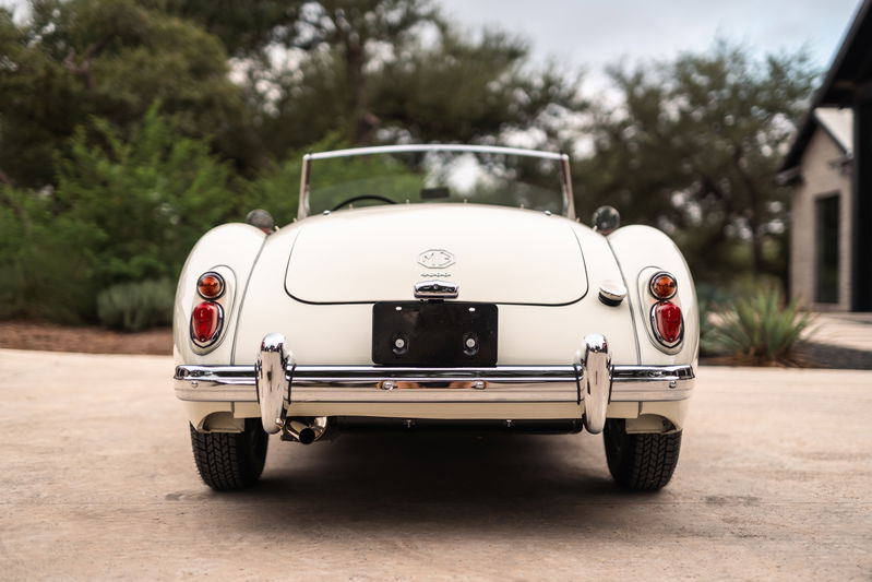 Rear view of a classic white 1957 MG MGA convertible with chrome bumper and exhaust tips.