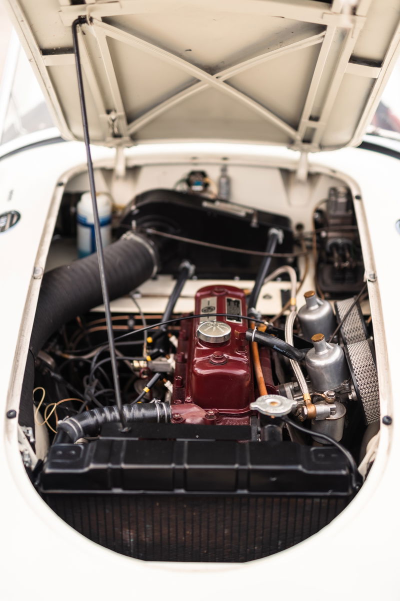 Close-up of the vintage MG MGA engine bay, featuring a maroon engine block, SU carburetors, and black air intake.