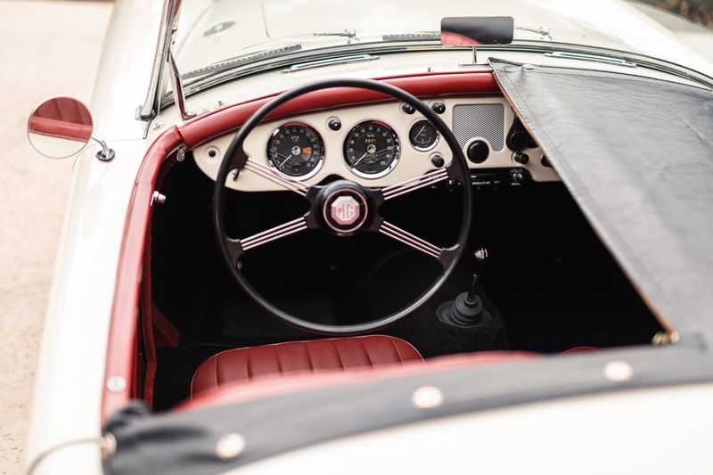 Interior of a 1957 MG MGA in Old English White with red trim and leather seats, featuring a classic dashboard.
