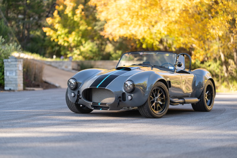 Gray 1965 Backdraft Cobra with dual blue racing stripes and black rims.