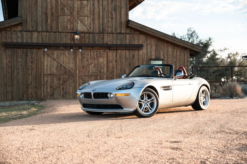 Silver 2002 BMW Z8 roadster with red interior, parked outside a rustic barn.
