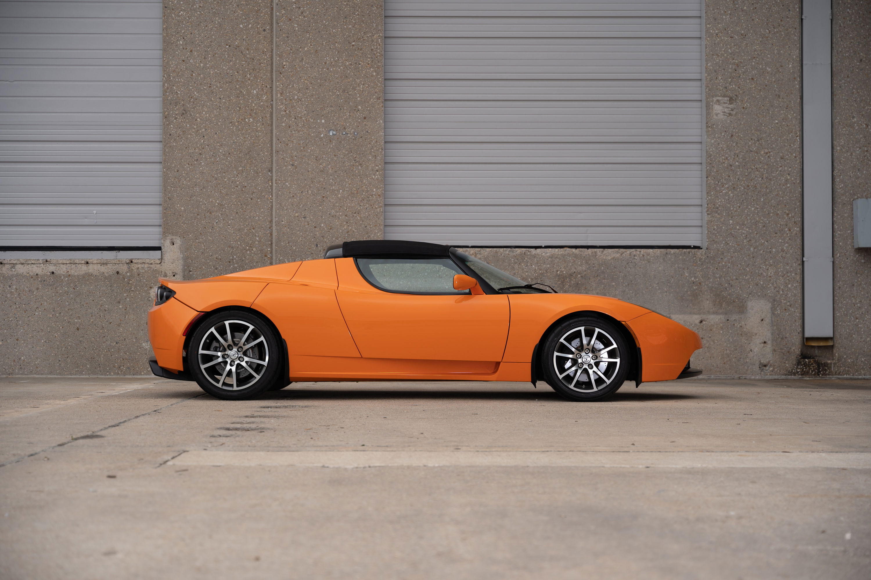Orange metallic 2010 Tesla Roadster with black soft top and silver rims.