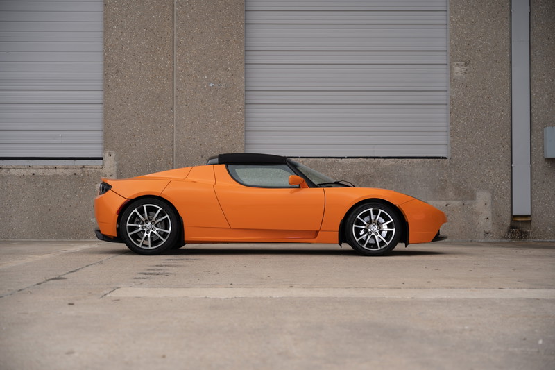 Orange metallic 2010 Tesla Roadster with black soft top and silver rims.