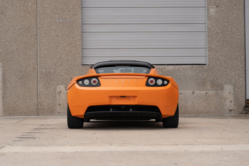 Rear view of an orange metallic 2010 Tesla Roadster, showcasing its taillights and black trim.