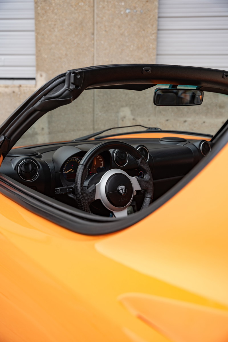 Orange 2010 Tesla Roadster interior. Close-up of the steering wheel and dashboard.