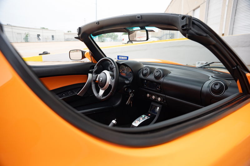 Interior of an orange 2010 Tesla Roadster with a black convertible top and dashboard.