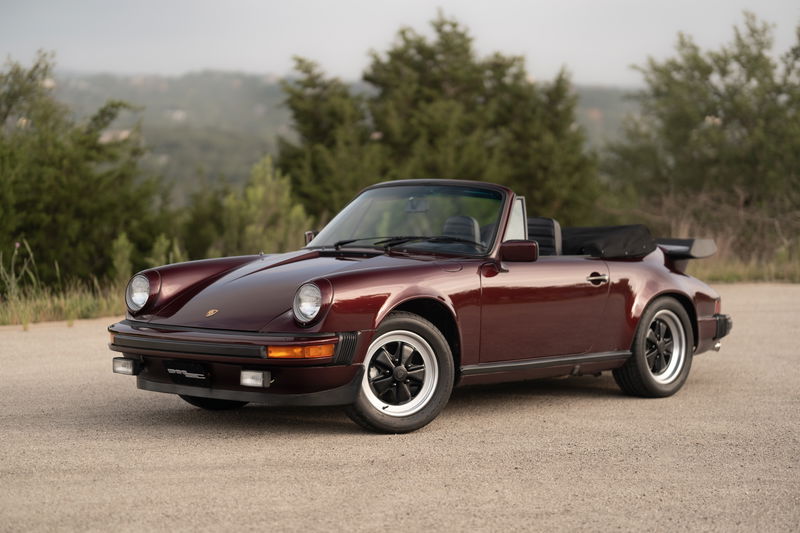 Ruby Red Metallic 1983 Porsche 911SC Cabriolet with black Fuchs rims and whale tail spoiler.
