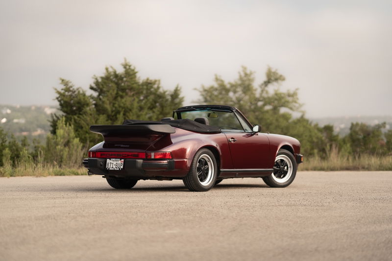 Rear view of a ruby red metallic 1983 Porsche 911 SC Cabriolet with whale tail spoiler and black trim.