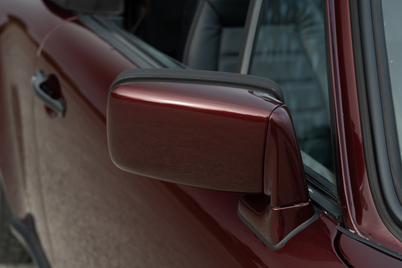 Close-up of a ruby red metallic 1983 Porsche 911SC Cabriolet, featuring the side mirror and door panel.
