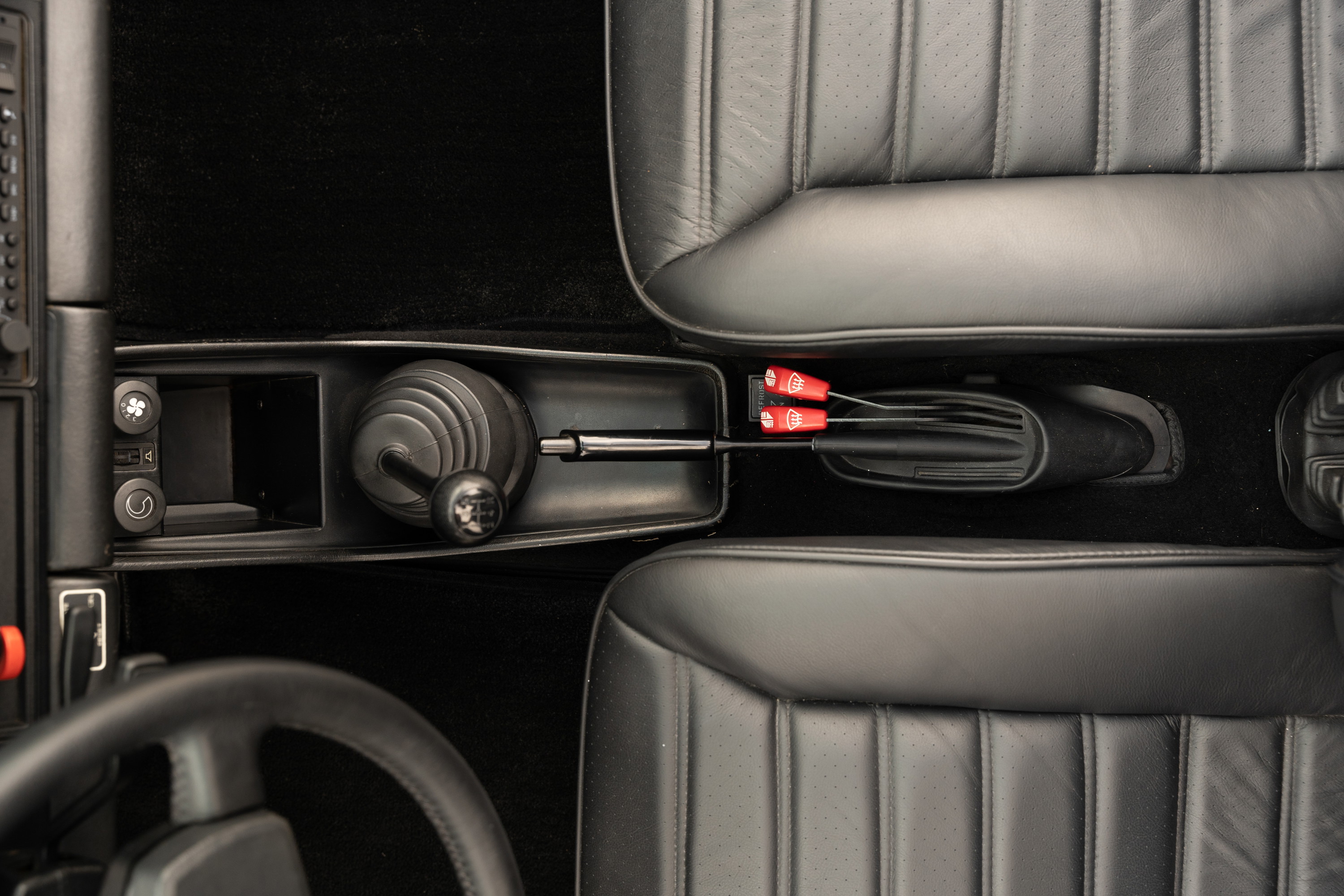 Close-up of a 1983 Porsche 911 SC Cabriolet interior, showing a manual shifter and black leather seats.