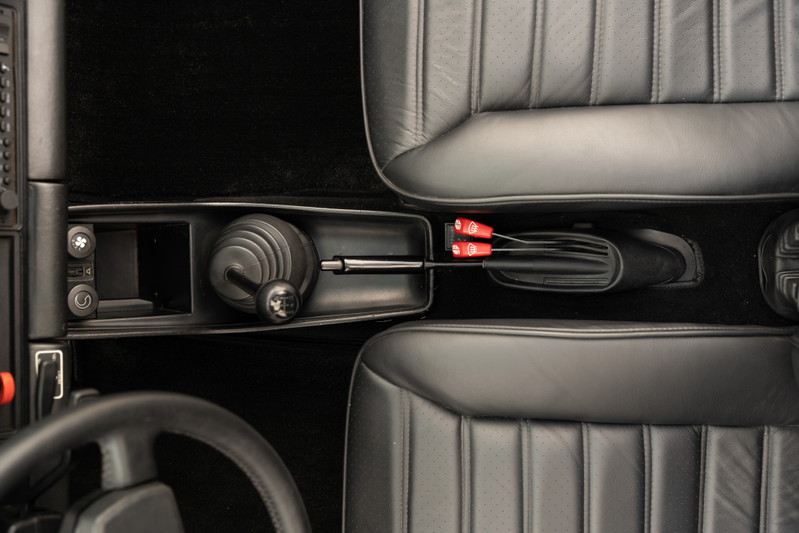 Close-up of a 1983 Porsche 911 SC Cabriolet interior, showing a manual shifter and black leather seats.