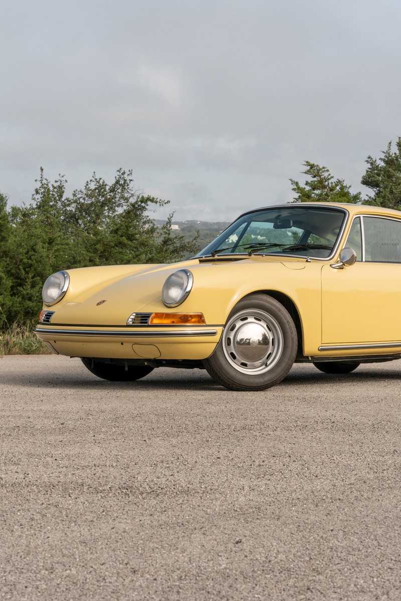 Close-up of a champagne yellow 1969 Porsche 912 coupe front fender, showing chrome trim and hubcaps.