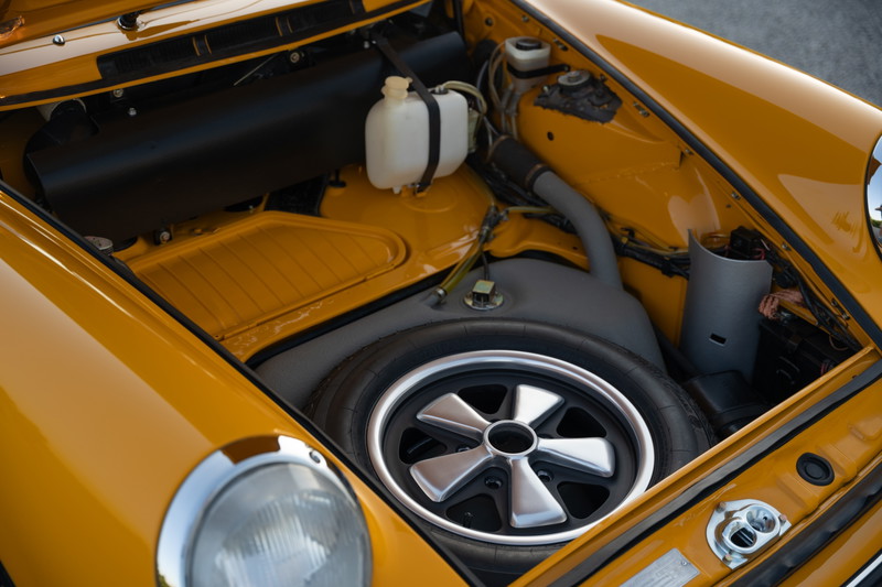 Front trunk of a Signal Yellow 1973 Porsche 911S Targa, showing spare tire and silver alloy rims.