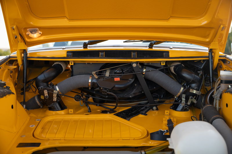Yellow 1973 Porsche 911S Targa engine bay with twin turbo intake piping.