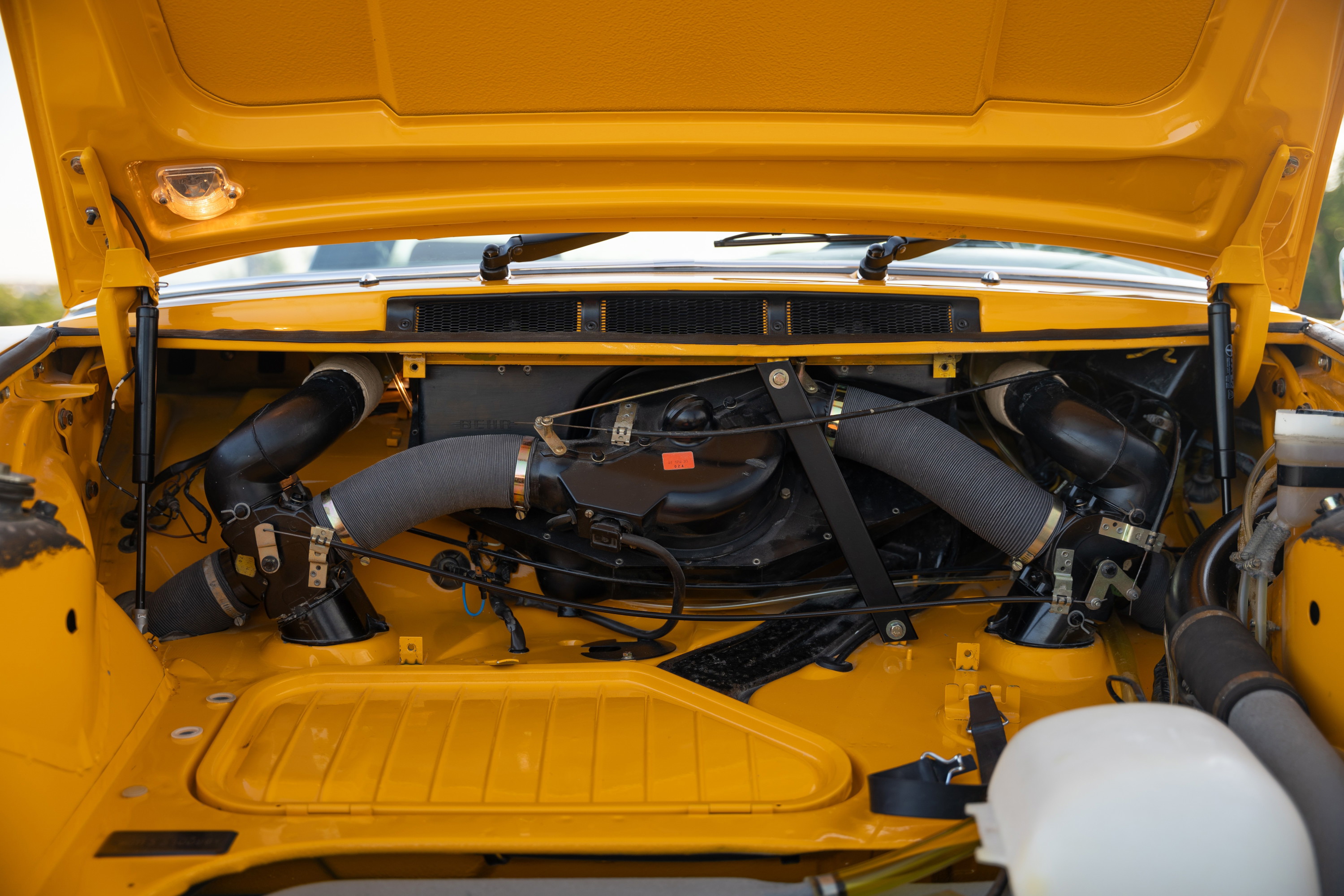 Yellow 1973 Porsche 911S Targa engine bay with twin turbo intake piping.