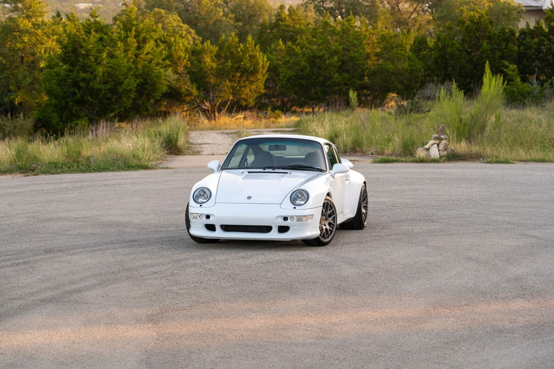 White 1997 Porsche 993 C4S coupe with grey multi-spoke rims parked on asphalt.