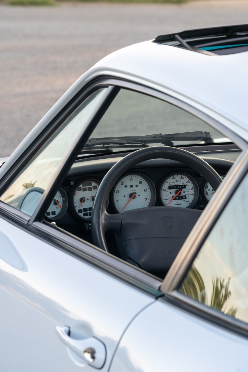 Interior view of a 1997 Porsche 993 C4S in Glacier White, showing the dashboard gauges and steering wheel.