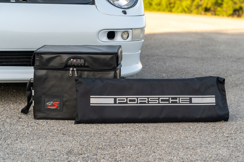 Black Porsche tool bags with silver accents and the Porsche script logo sit beside a white 1997 Porsche 993 C4S.