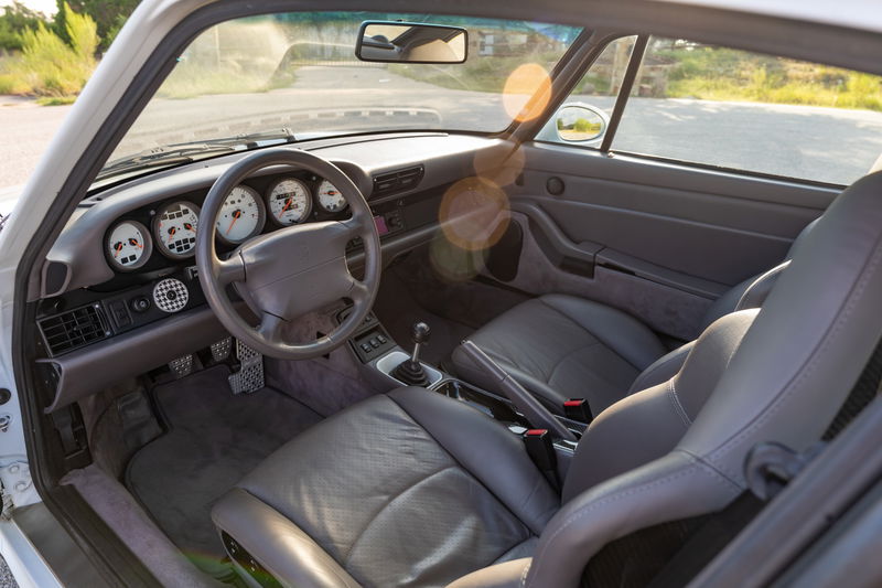 Interior of a Glacier White 1997 Porsche 993 C4S showing gray leather seats and the instrument cluster.