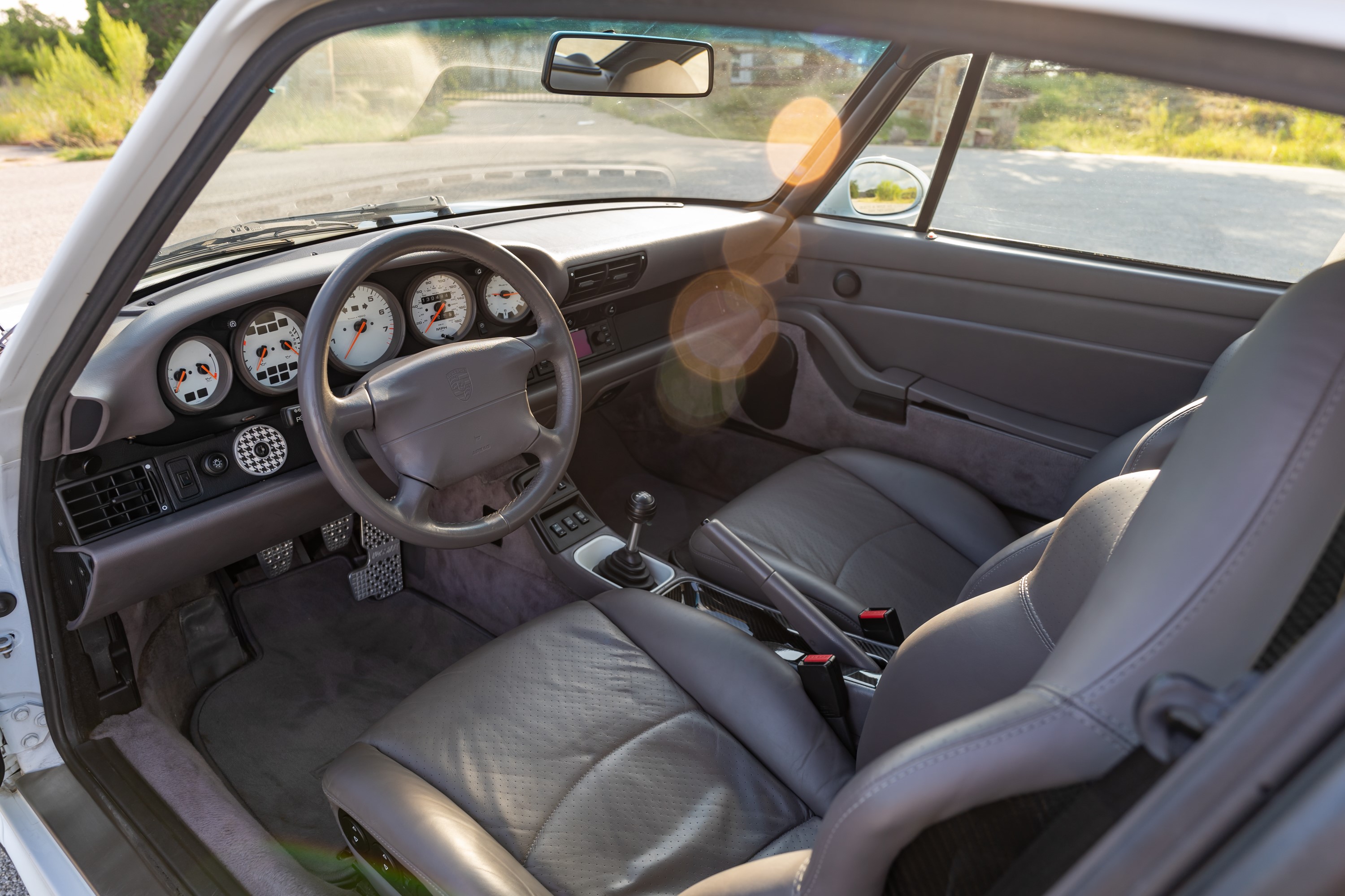 Interior of a Glacier White 1997 Porsche 993 C4S showing gray leather seats and the instrument cluster.