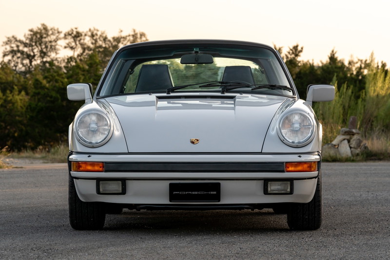 Front view of a white 1987 Porsche 911 Carrera Targa with black trim and fog lights.