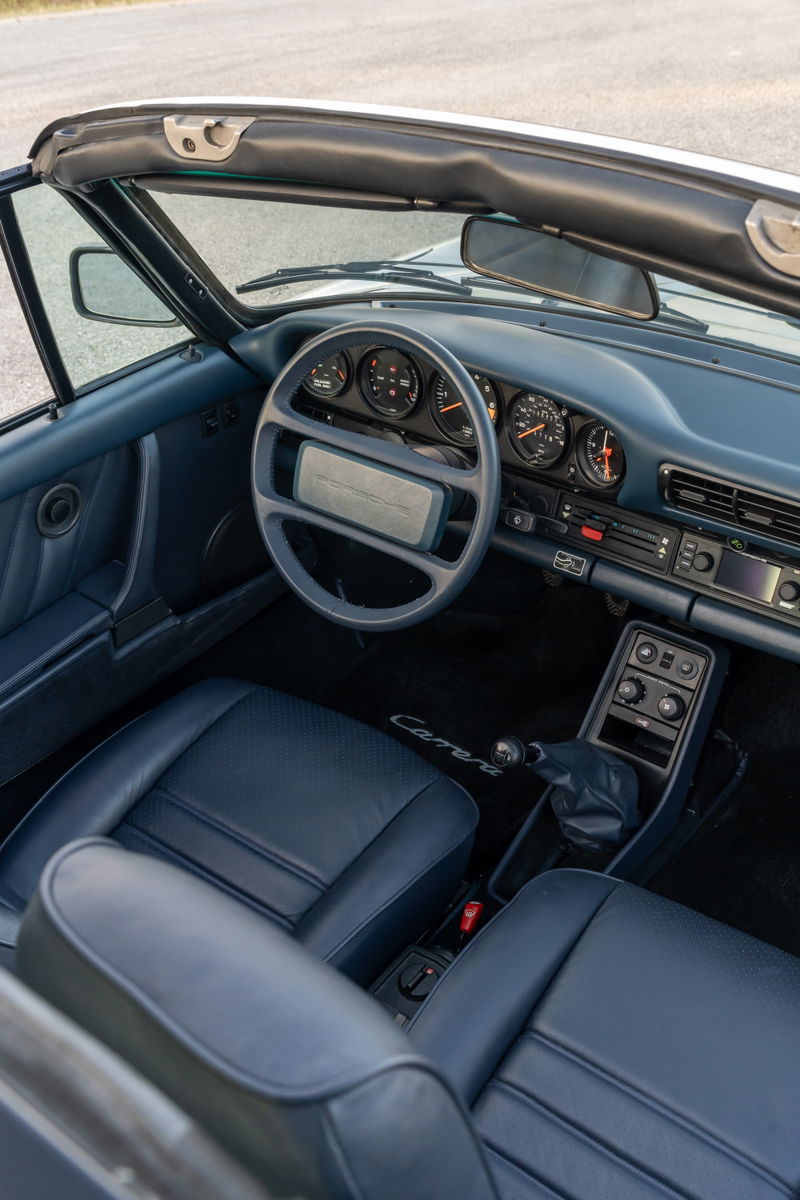 Interior view of a 1987 Porsche 911 Carrera Targa in Marble Grey with blue leather seats and dashboard.