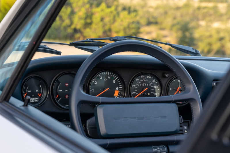 1987 Porsche 911 Carrera Targa interior with analog gauges and leather-wrapped steering wheel.