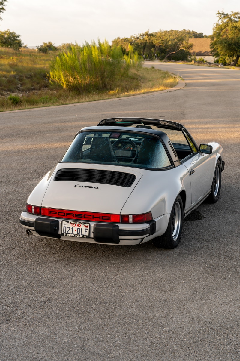 Rear view of a white 1987 Porsche 911 Carrera Targa with black rims and targa top.